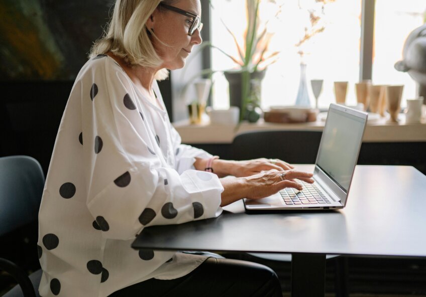 Kvinde med briller arbejder på en bærbar computer ved et bord i et lyst rum.