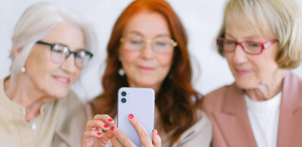 Tre ældre kvinder ser på en smartphone sammen og smiler.