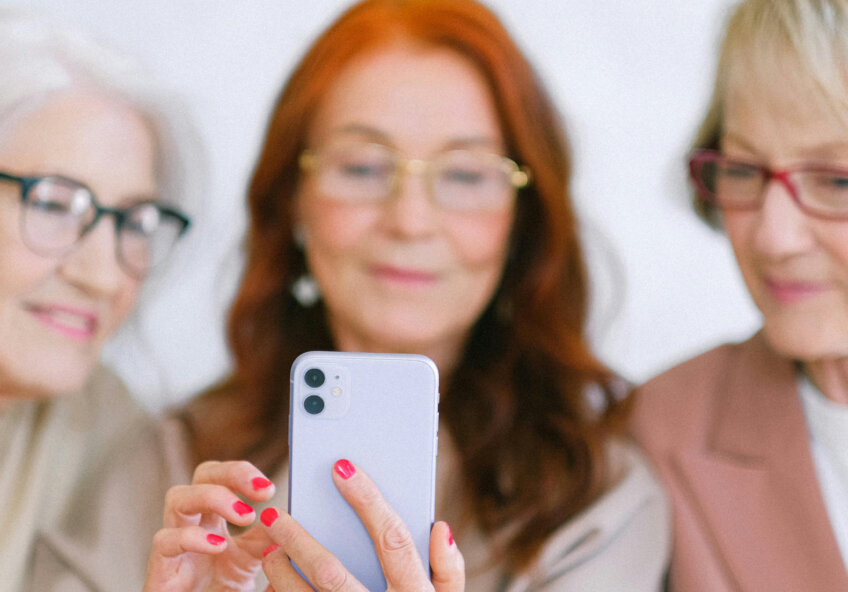 Tre ældre kvinder ser på en smartphone sammen og smiler.