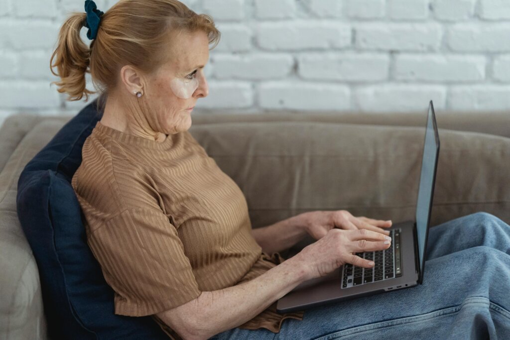 Ældre kvinde sidder på en sofa og bruger en bærbar computer, fokuseret og engageret.