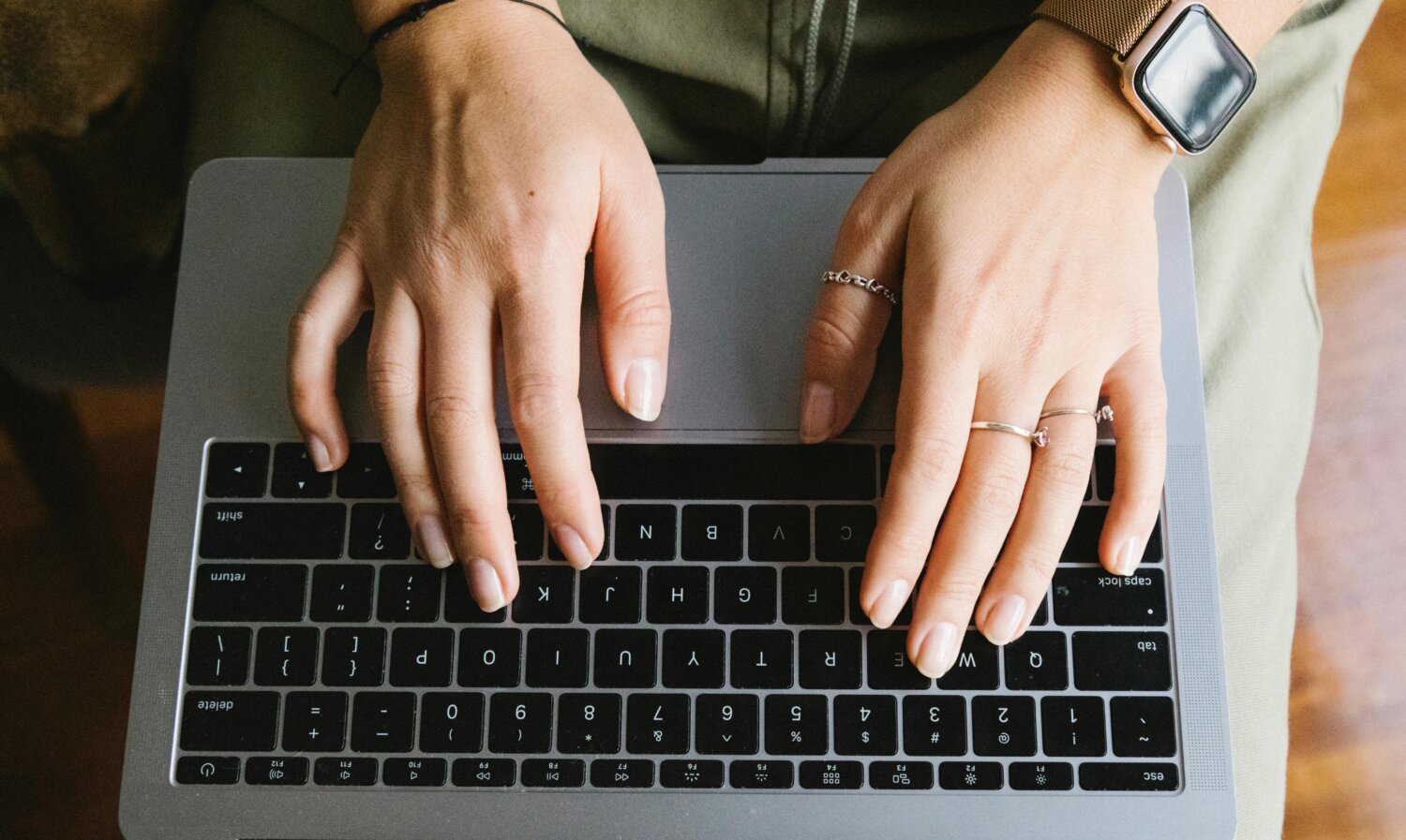 Nærbillede af hænder, der skriver på en laptop, fokuseret på tastaturet med smykker og smartwatch.