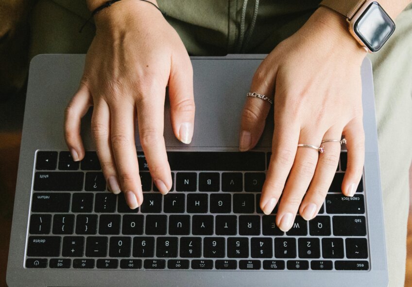 Nærbillede af hænder, der skriver på en laptop, fokuseret på tastaturet med smykker og smartwatch.