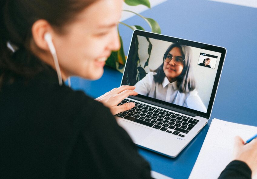 Kvinde med øretelefoner deltager i et videomøde på en bærbar computer med en anden kvinde, mens hun tager noter.