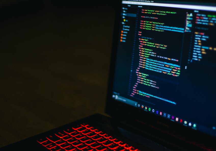 Laptop med oplyst tastatur viser HTML-kode i en kodeeditor på skærmen.